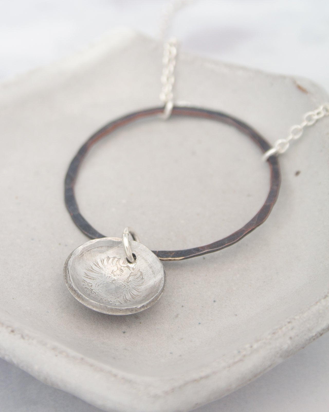 A silver necklace with a circular pendant and a metal ring around it, resting on a white surface.