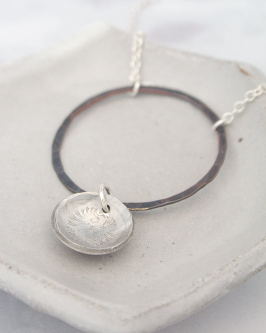 A silver necklace with a circular pendant and a metal ring around it, resting on a white surface.