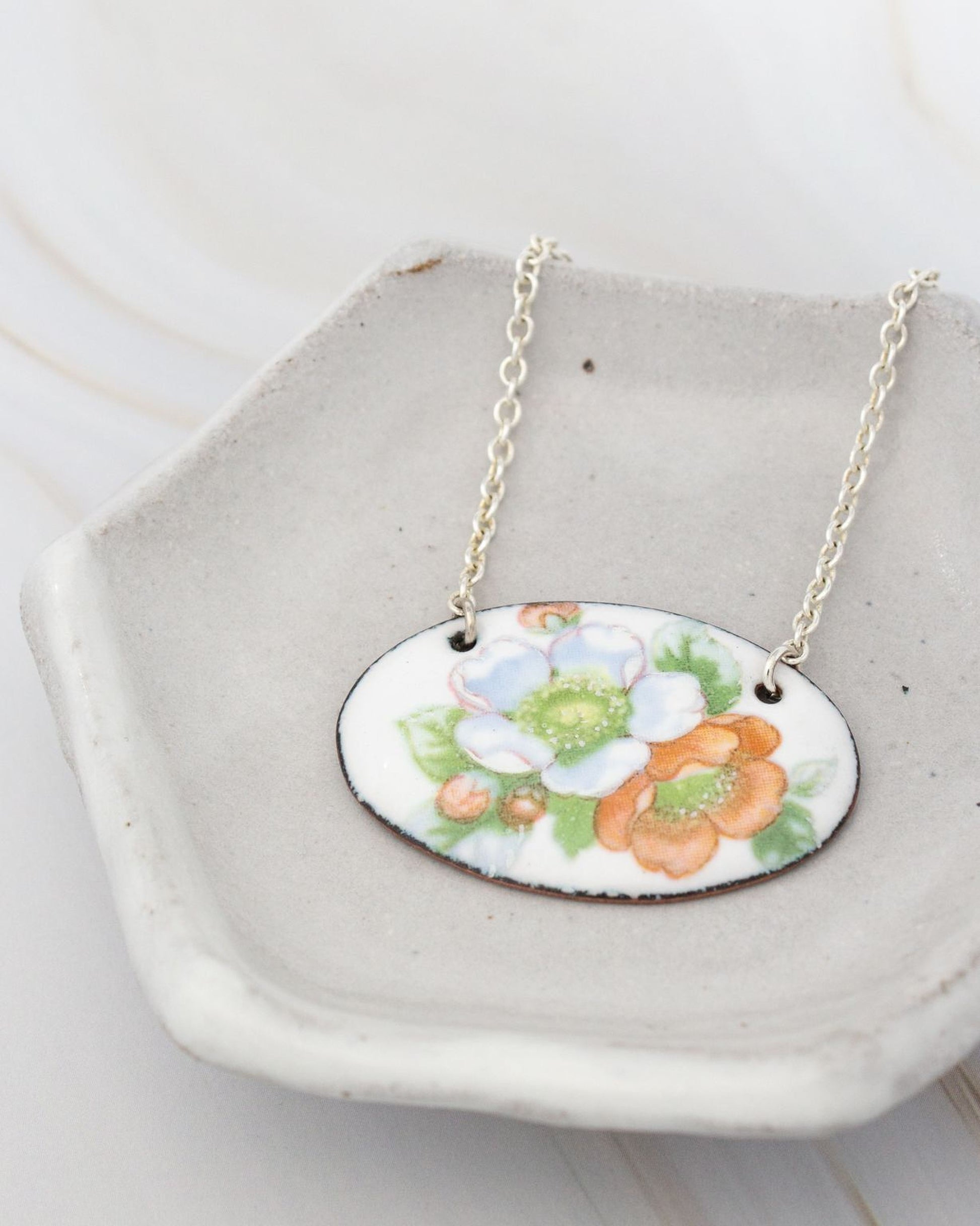 A necklace with a pendant featuring a floral design is displayed on a white ceramic dish.