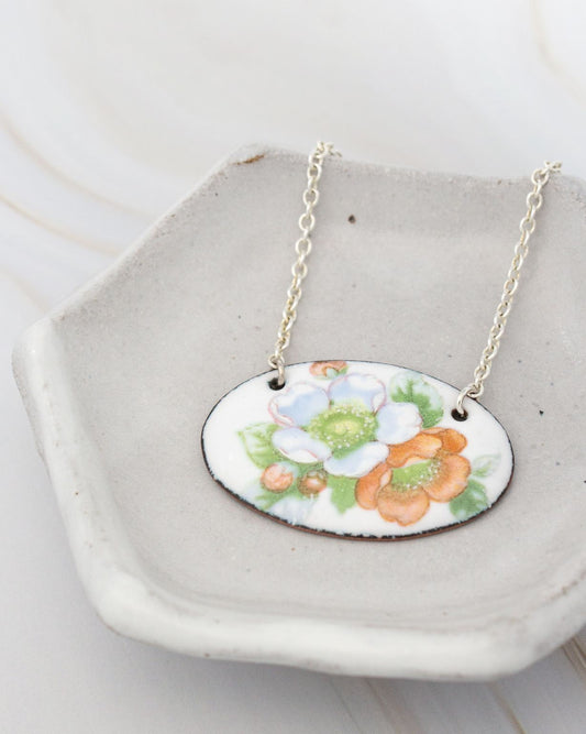 A necklace with a pendant featuring a floral design is displayed on a white ceramic dish.