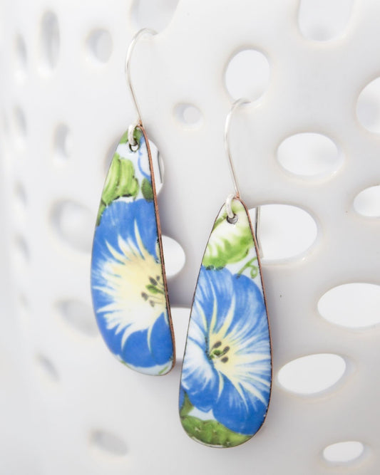 A pair of earrings with blue and white floral designs, hanging from a hook against a white background.