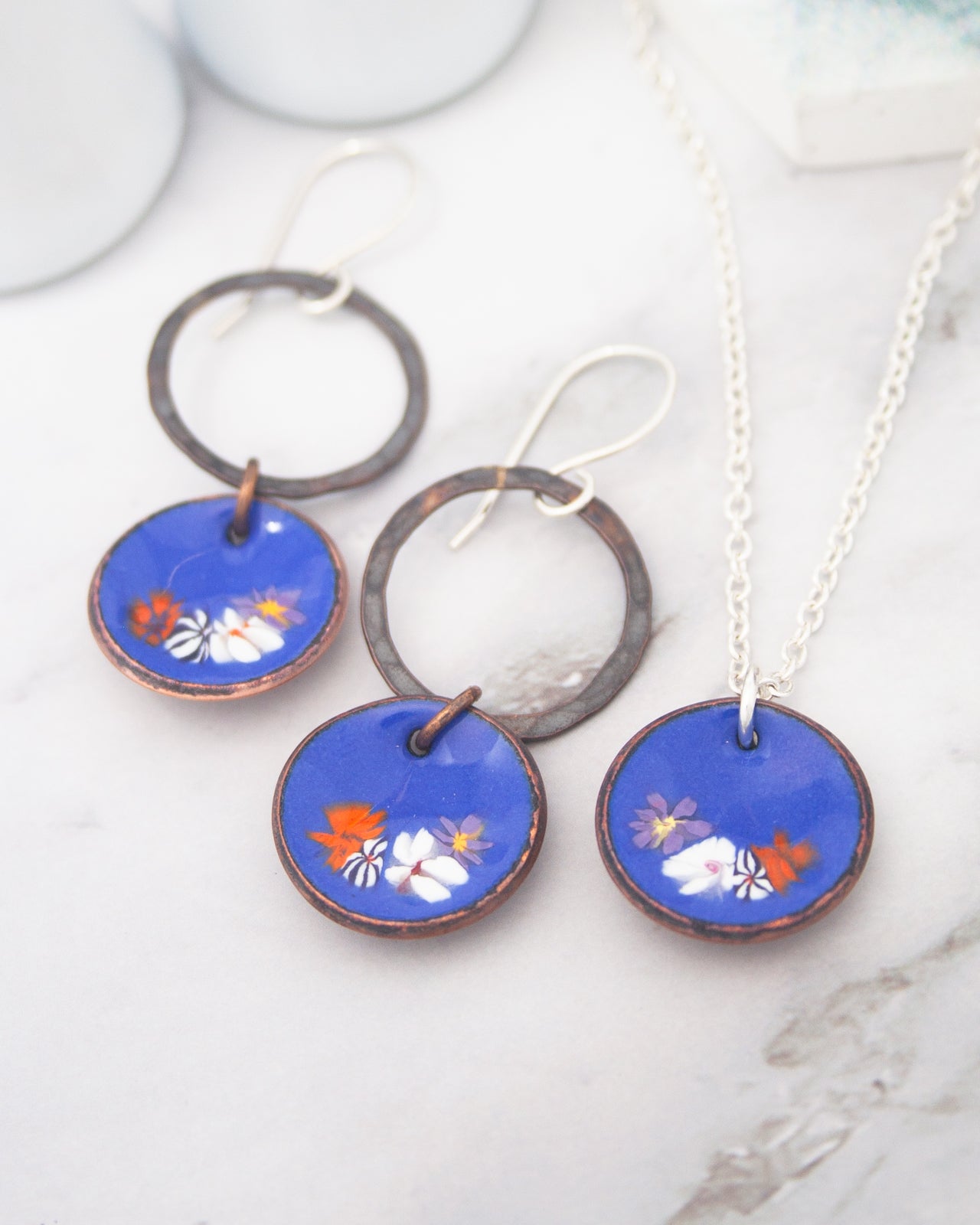 a pair of blue earrings and a necklace with floral designs.