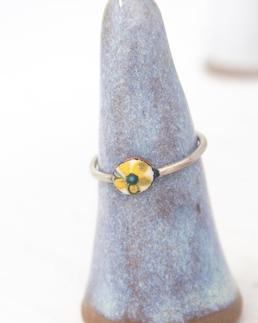 A ring with a yellow and green floral design is displayed on a blue ceramic stand.