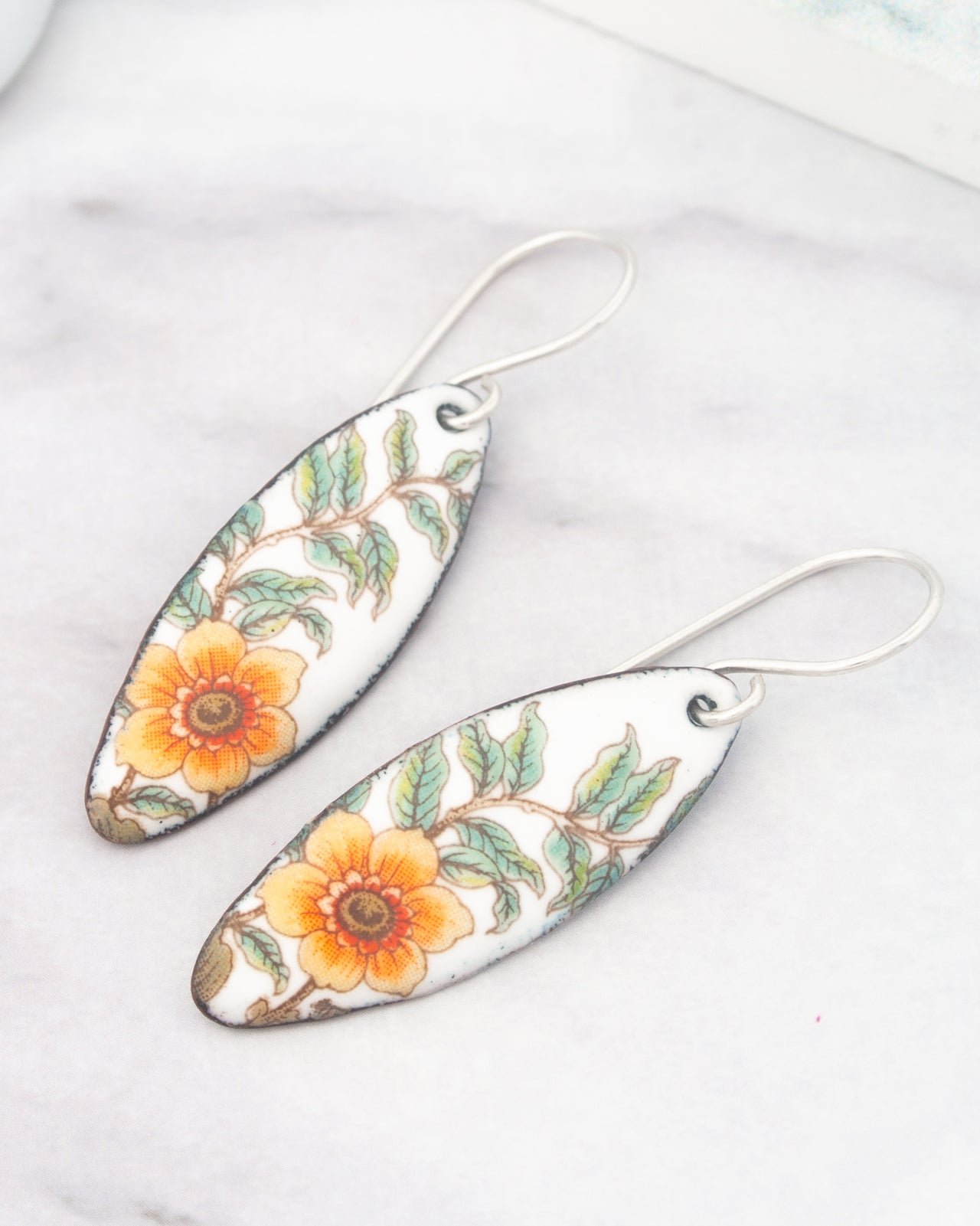 A pair of earrings with a floral design, featuring orange and green flowers on a white background.