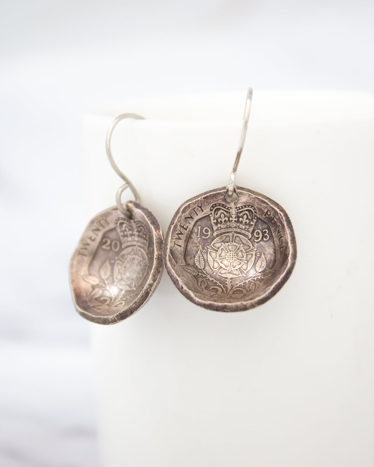 A pair of silver earrings made from a coin, featuring the words "TWENTY" and "1993" engraved on them.