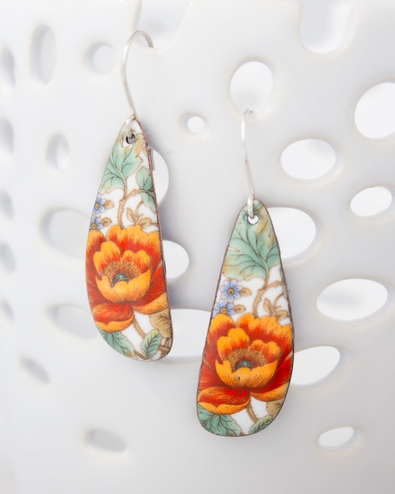 A pair of earrings with a floral design, featuring vibrant orange and red flowers against a white background.
