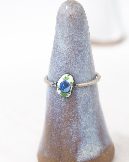 A ring with a blue flower design on it, displayed on a ceramic stand.