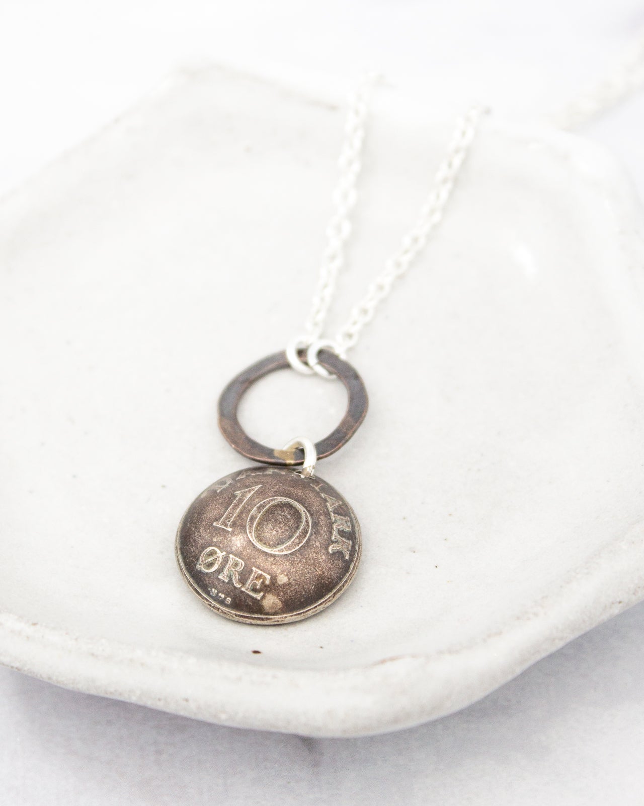 A necklace with a pendant in the shape of a 10-cent coin, hanging from a chain.