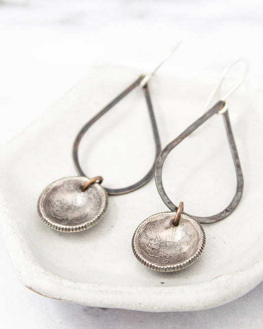 A pair of silver earrings with metal pendants hanging from a metal frame.