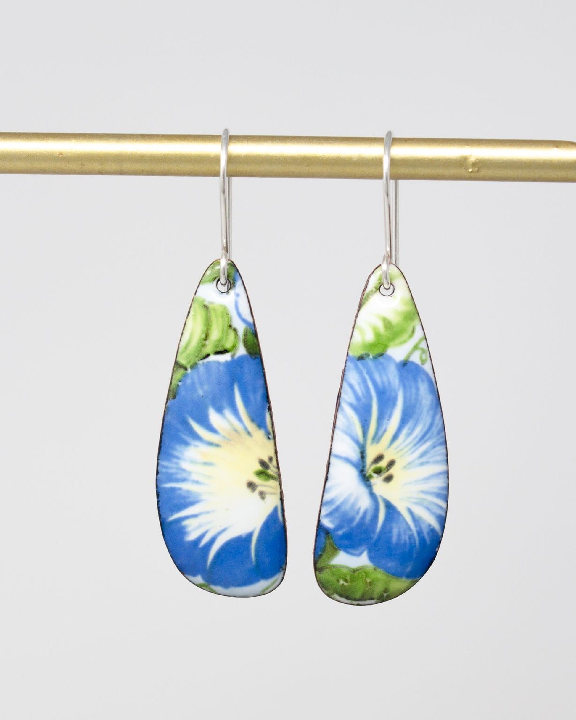 A pair of earrings with blue and white floral designs hanging from a gold bar.