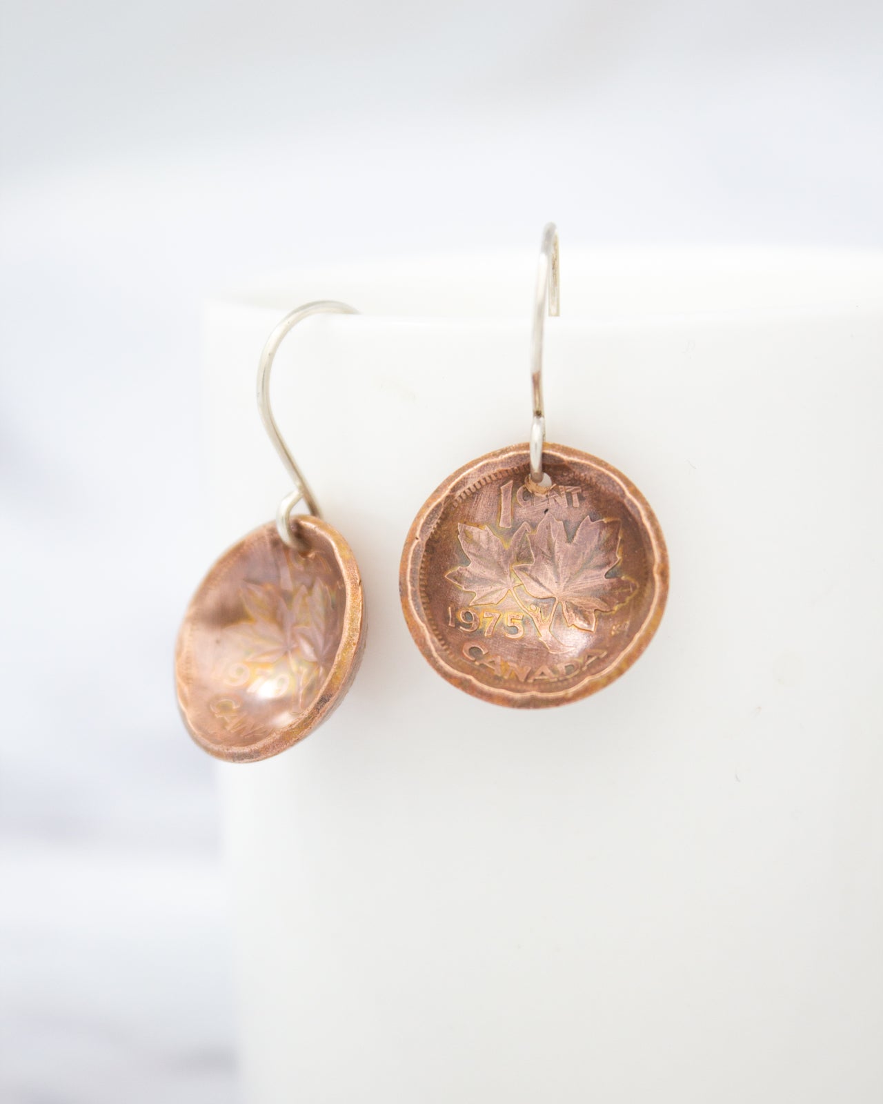 a pair of copper-colored earrings with leaf designs, hanging from a hook against a white background.