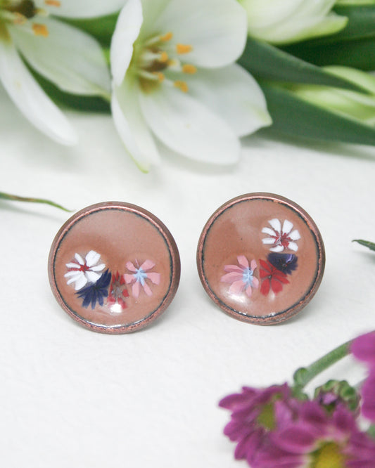 a close up of a pair of earrings with flowers in the background
