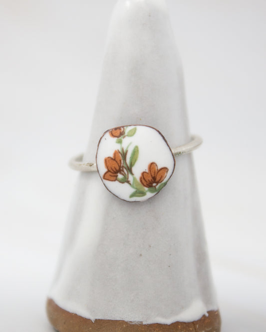 A white ceramic ring with a floral design on it, placed on a white pedestal.