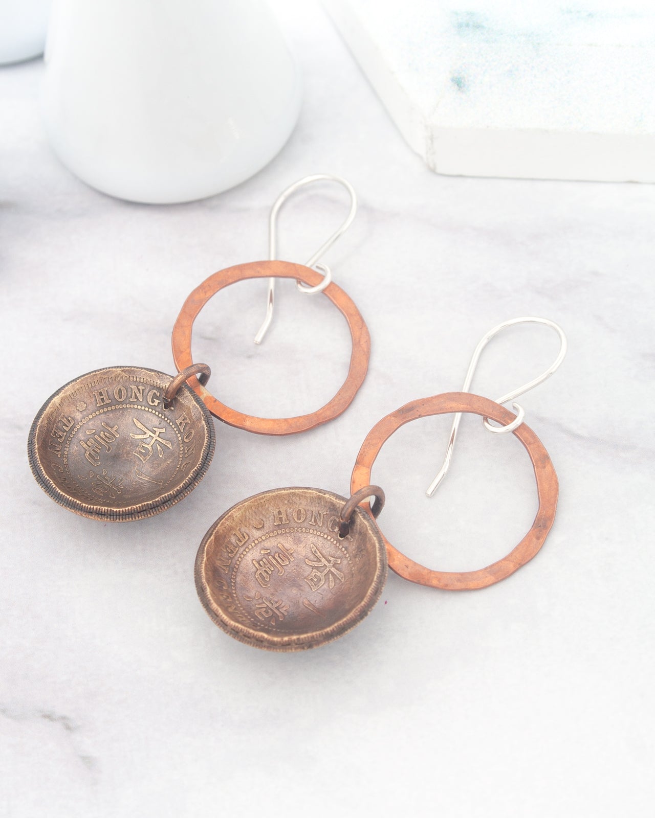 a pair of earrings with a combination of copper and brass materials, featuring a circular design with a metallic ring and a round metal pendant.