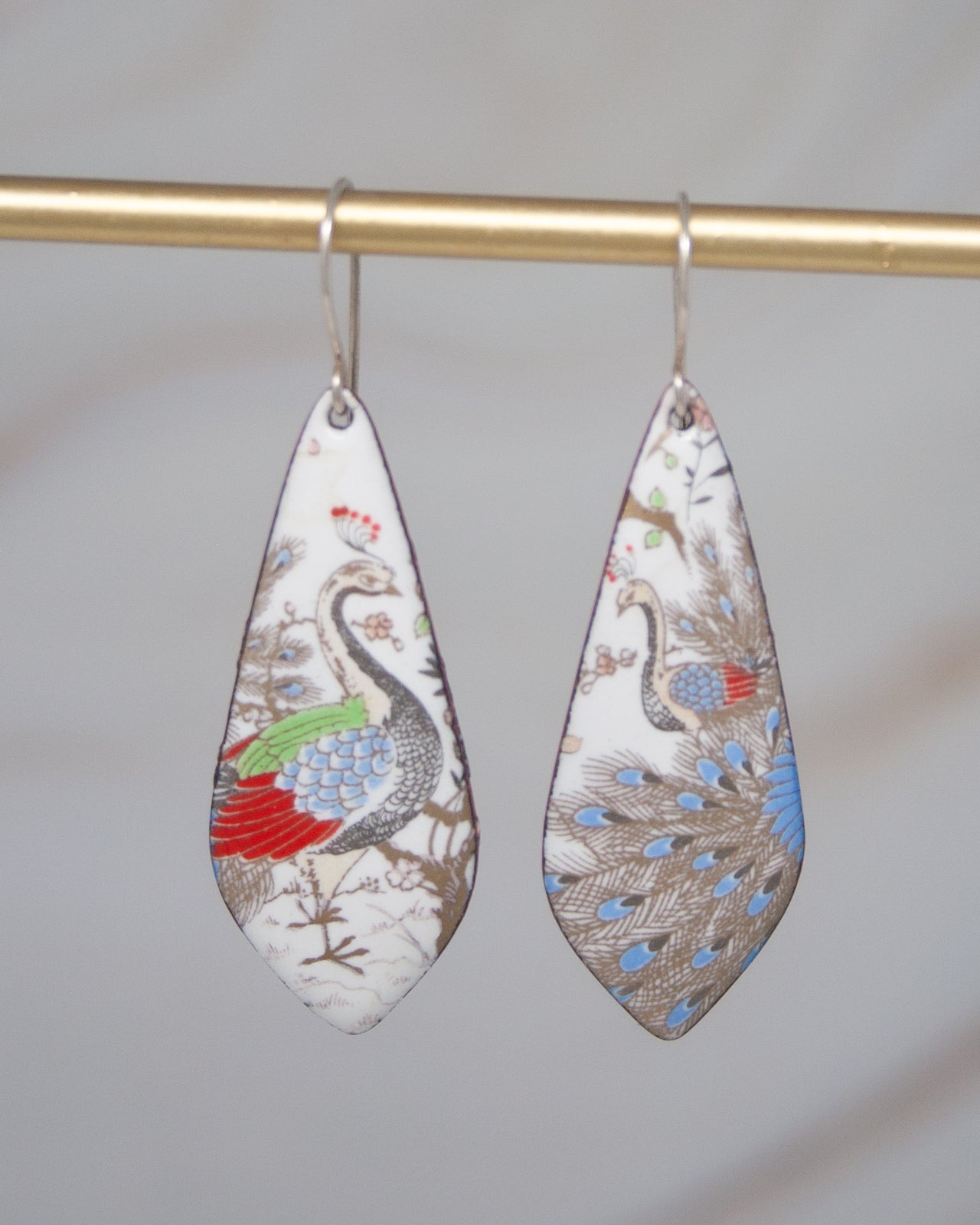 A pair of earrings with a colorful, abstract design featuring a bird-like figure in shades of blue, green, and red.