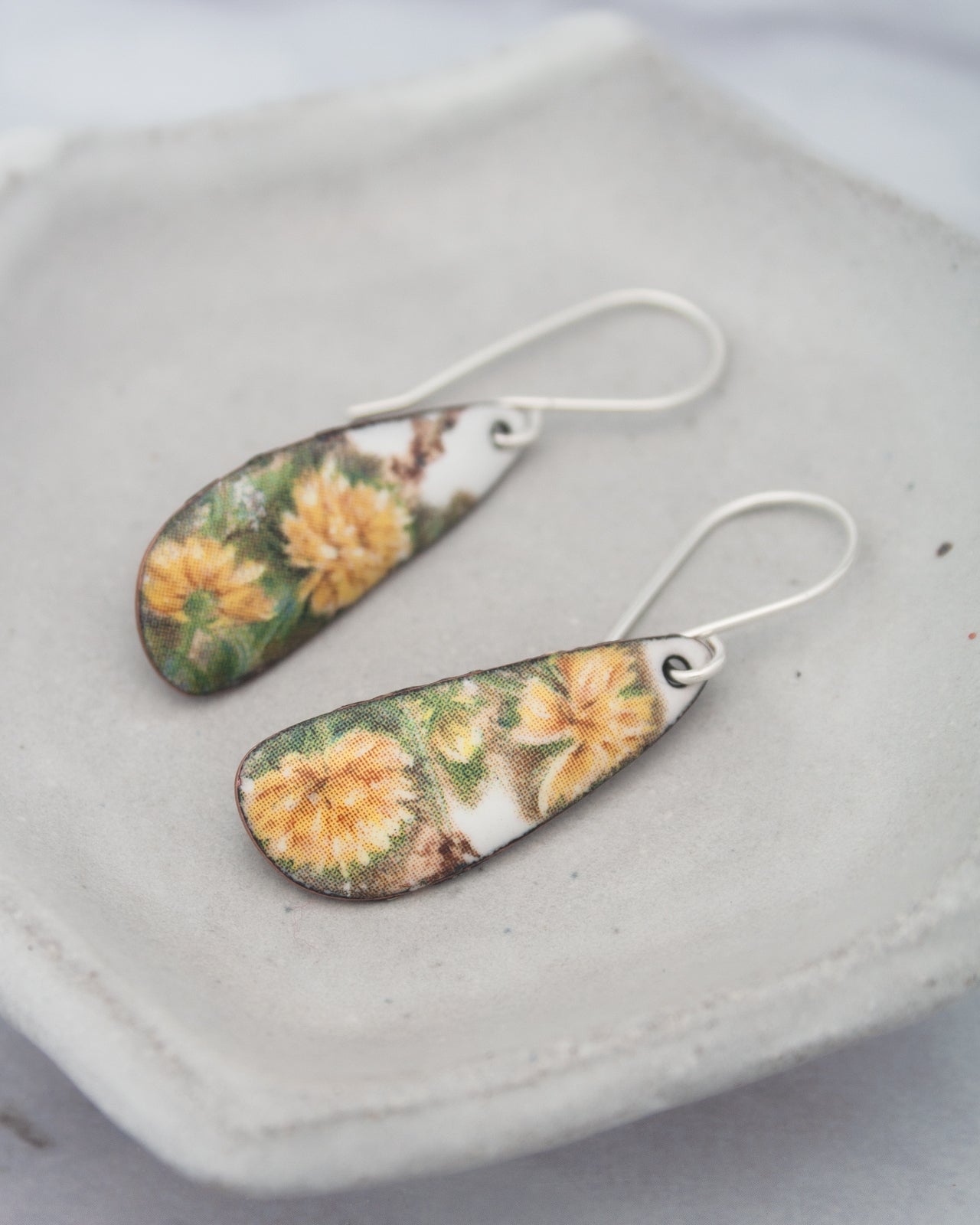 A pair of earrings with a floral design, featuring yellow flowers on a white background.