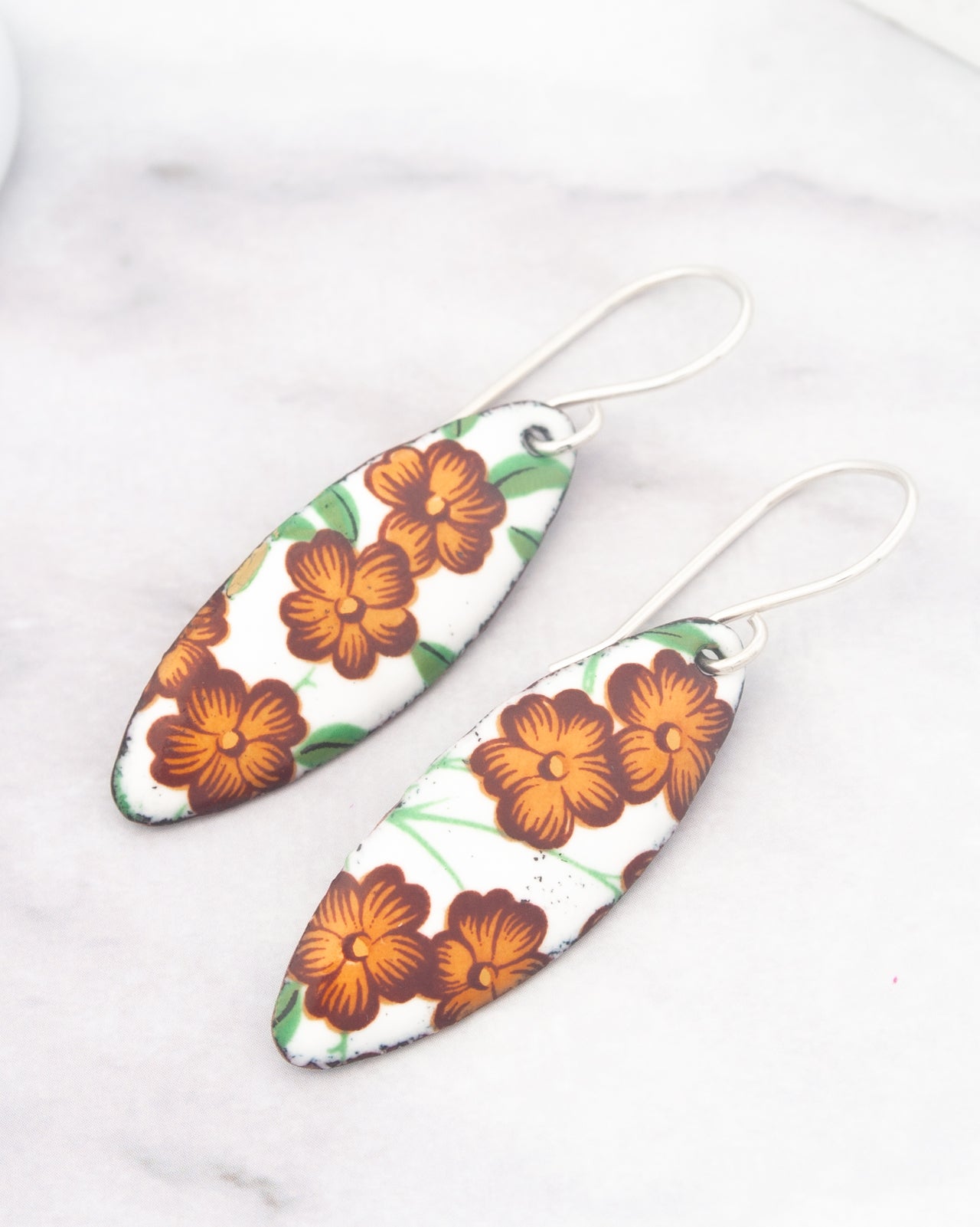 a pair of earrings with a floral design, featuring orange flowers on a white background.