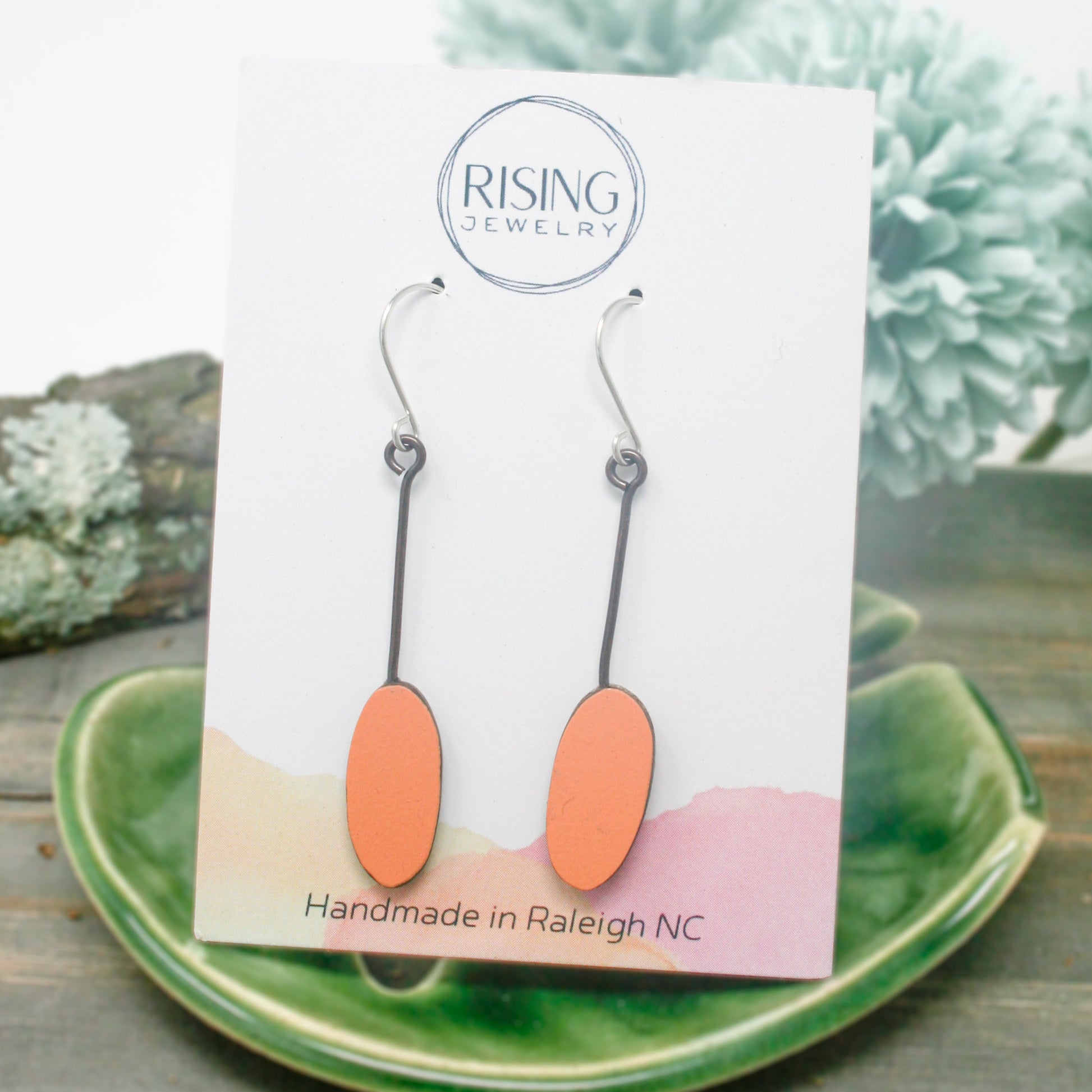 a pair of orange and silver earrings sitting on top of a green plate