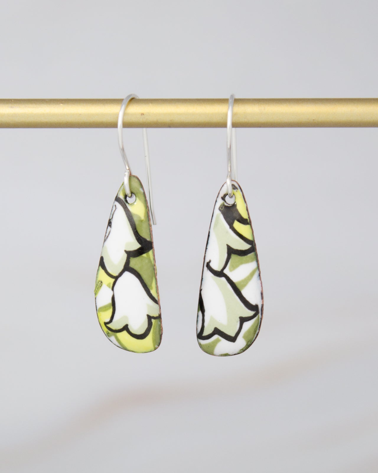 A pair of earrings with a floral pattern on a gold bar.
