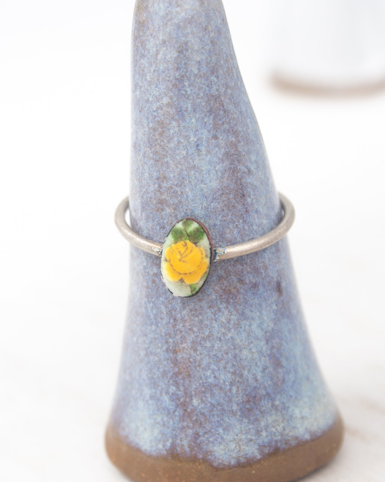 A ring with a yellow flower on it, displayed on a blue ceramic stand.