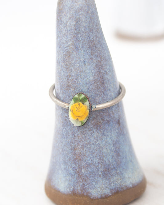 A ring with a yellow flower on it, displayed on a blue ceramic stand.