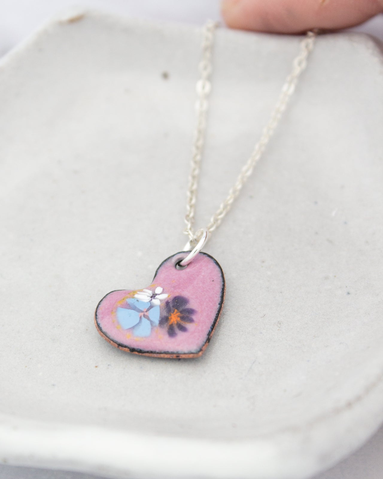 A heart-shaped pendant with a floral design is displayed on a white surface.