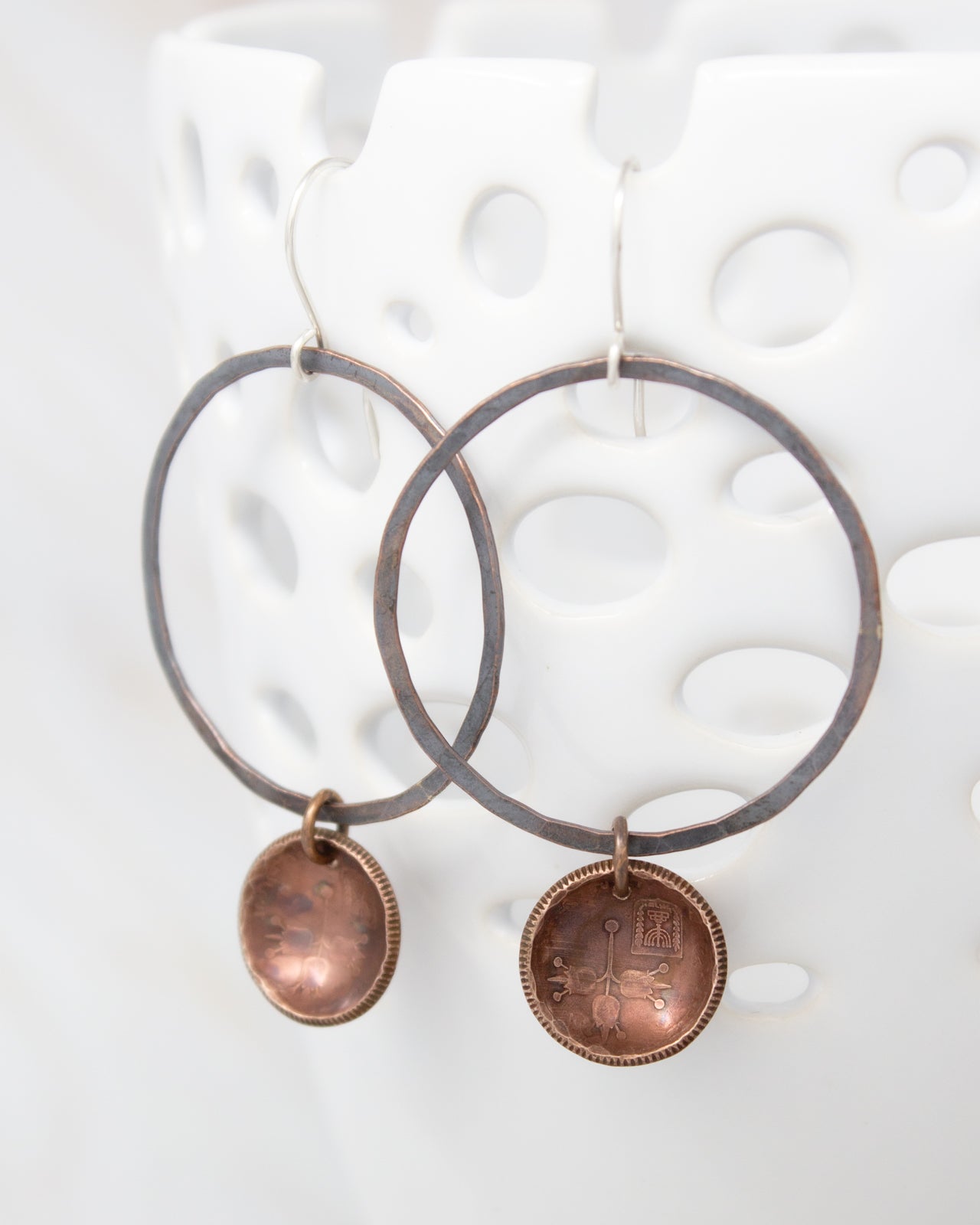 A pair of earrings with a circular metal frame and a small metal pendant hanging from it.