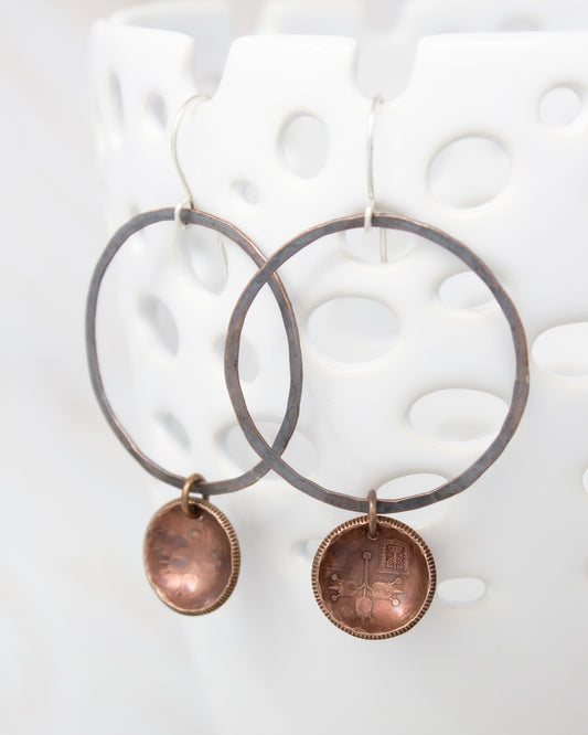 A pair of earrings with a circular metal frame and a small metal pendant hanging from it.
