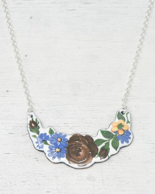 A necklace with a pendant featuring a floral design, including blue and brown flowers and leaves.