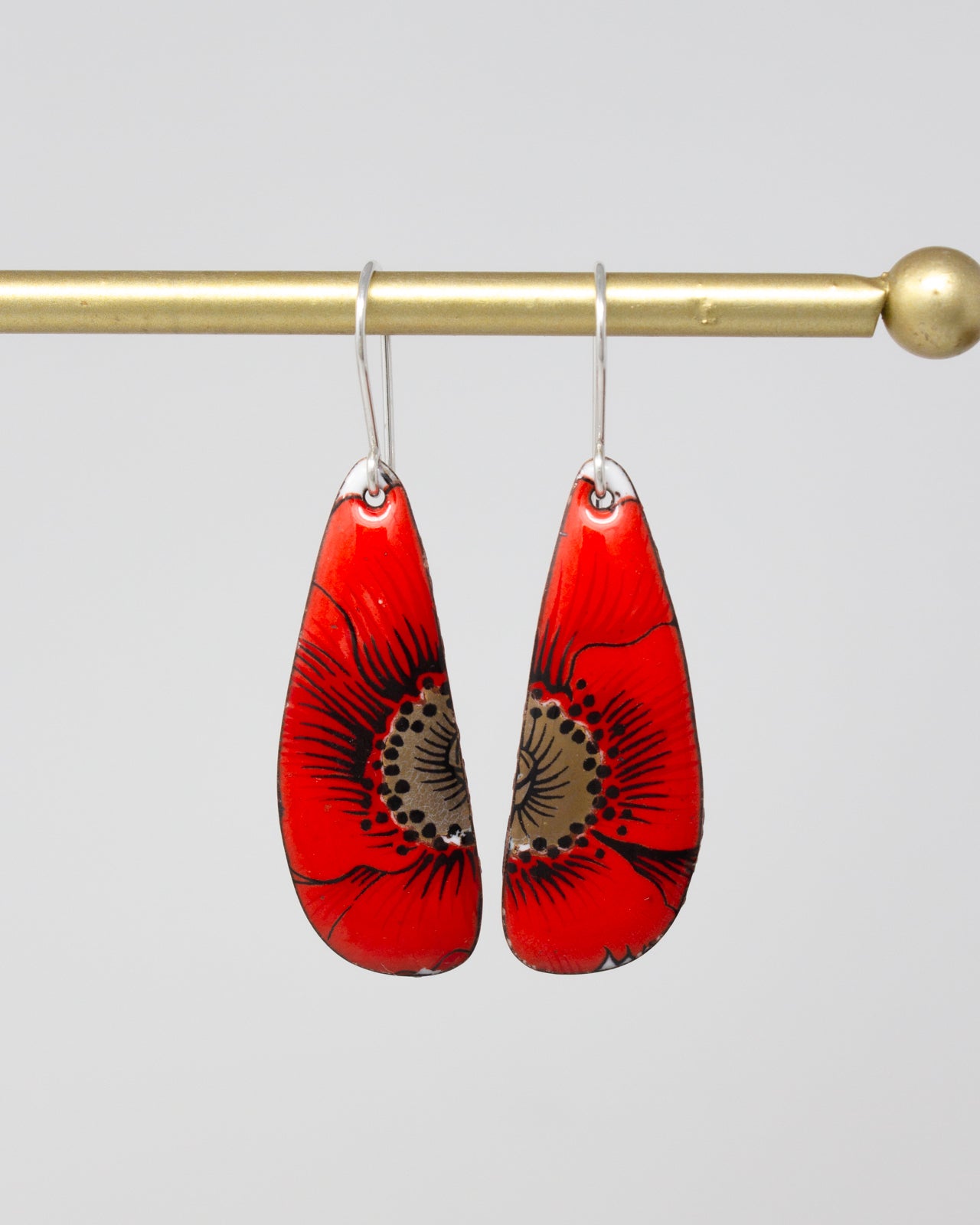 A pair of red earrings with black floral designs hanging from a gold-colored metal hook.