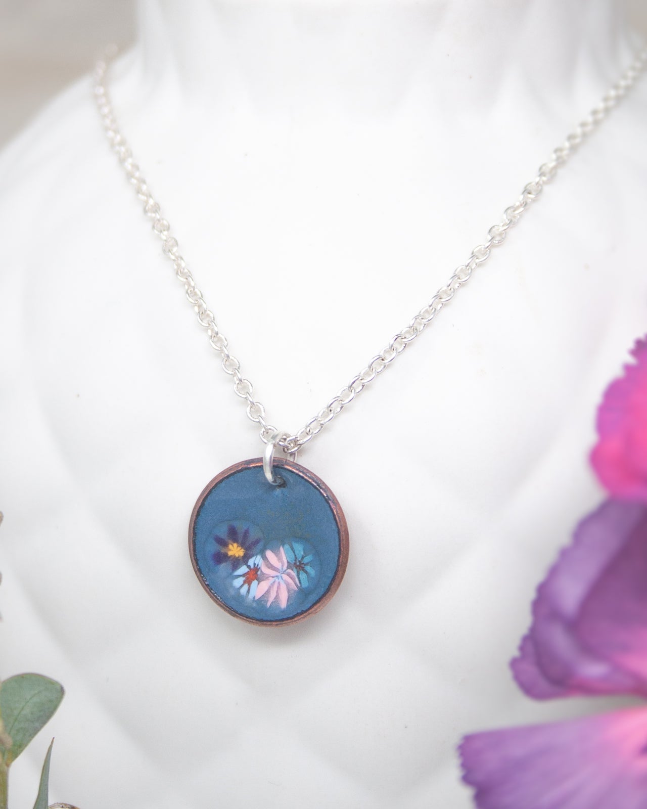A necklace with a circular pendant featuring a floral design in blue and pink colors.