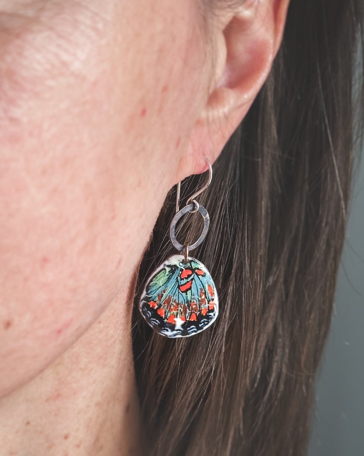 A close-up view of a person's ear wearing a pair of earrings with a colorful butterfly design.