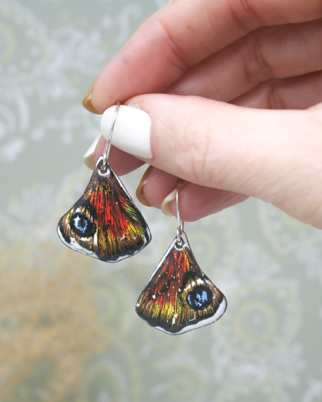 a hand holding a pair of earrings with a butterfly on it