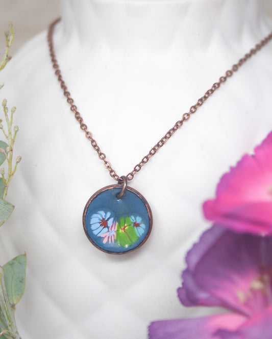 A necklace with a blue pendant featuring a floral design is displayed against a white background.