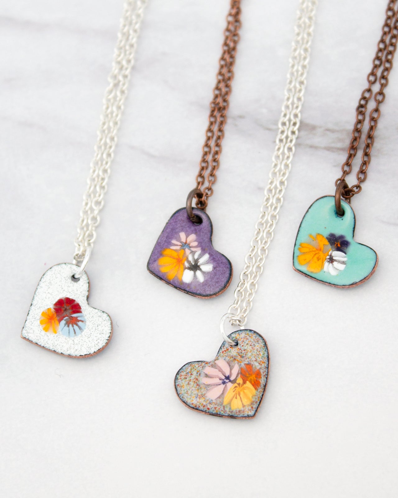 four heart-shaped pendants with different floral designs, each hanging from a chain.