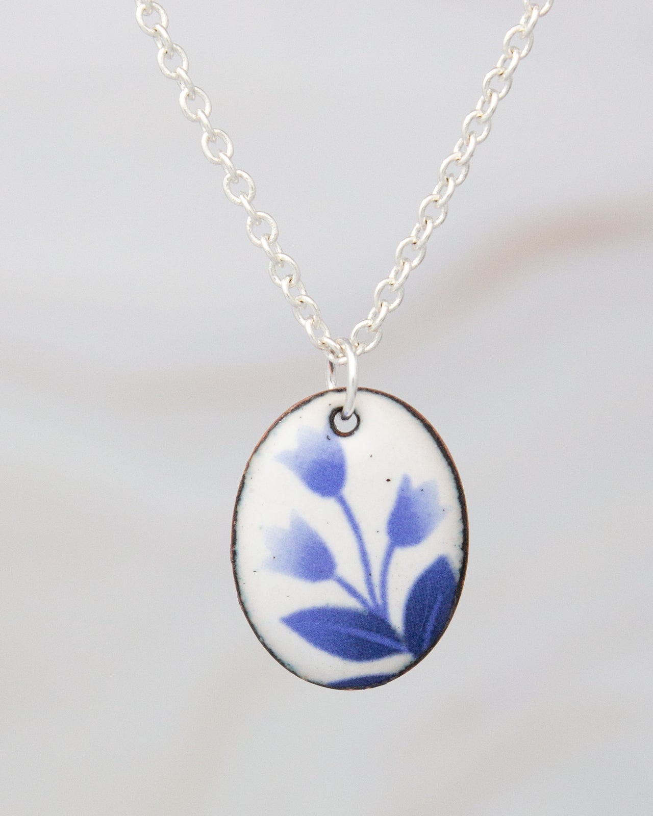 A silver necklace with a pendant featuring a blue floral design.
