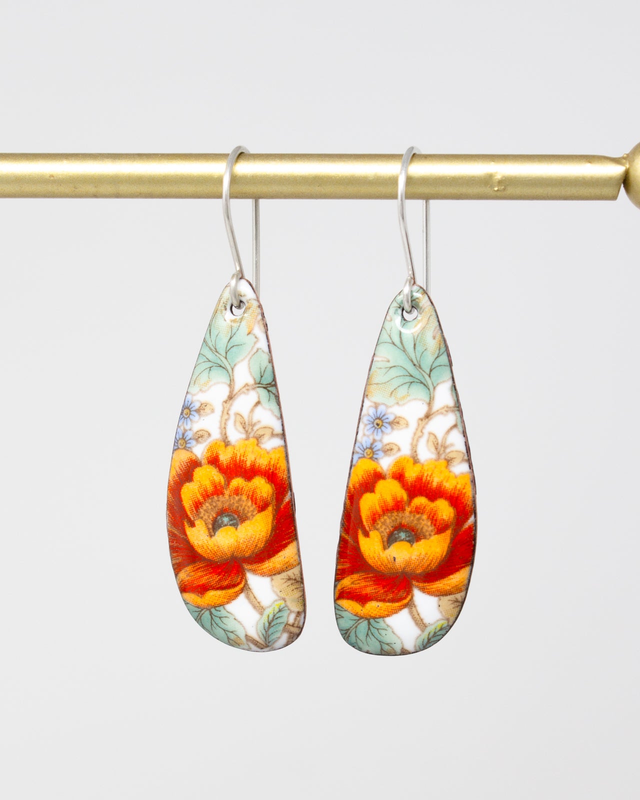 A pair of earrings with a floral design, featuring vibrant orange and red flowers against a white background.