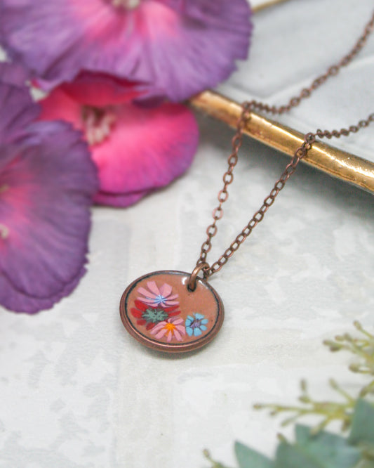A necklace with a circular pendant featuring a floral design, surrounded by purple and pink flowers.