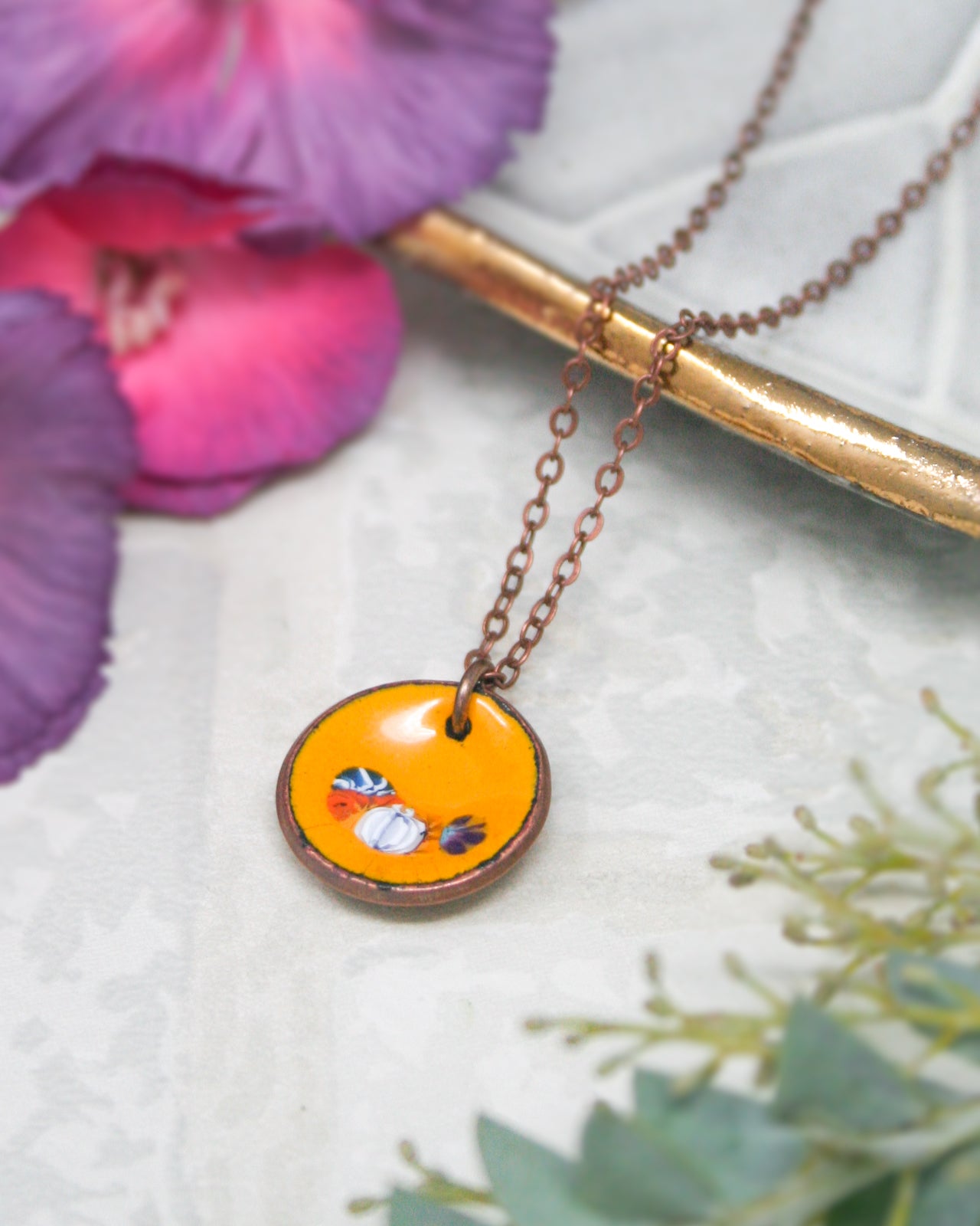 a necklace with a circular pendant, which appears to be a piece of jewelry. The pendant is surrounded by a chain and is placed on a surface with a floral background.