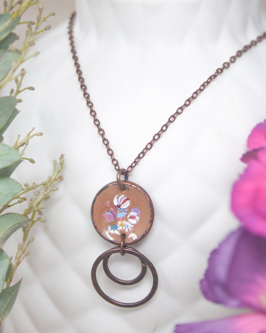 A necklace with a circular pendant featuring a floral design, hanging from a chain.
