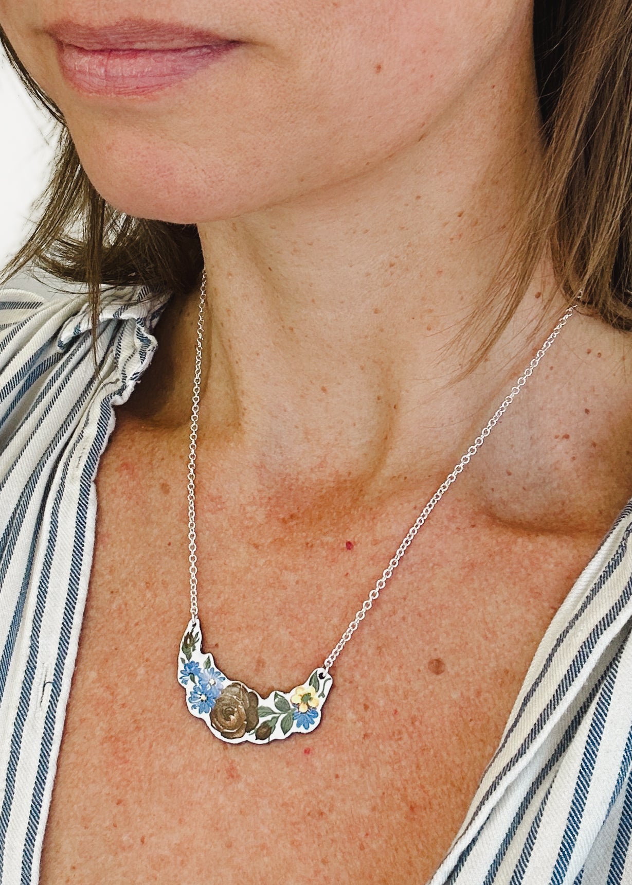 A close-up of a woman's neck and chest area, showing a delicate necklace with a floral pendant.