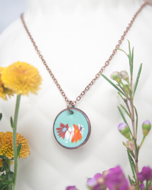 A necklace with a circular pendant featuring a floral design, surrounded by yellow flowers and purple flowers.