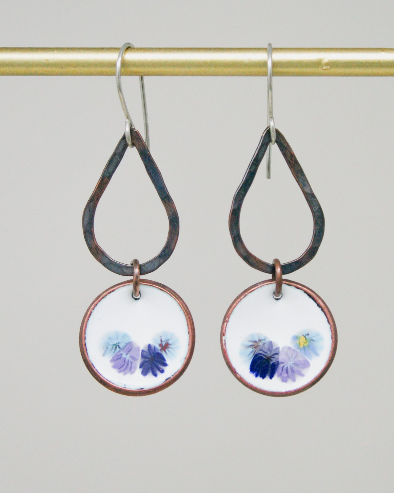 A pair of earrings with a floral design on the circular pendants hanging from a gold-colored metal hook.