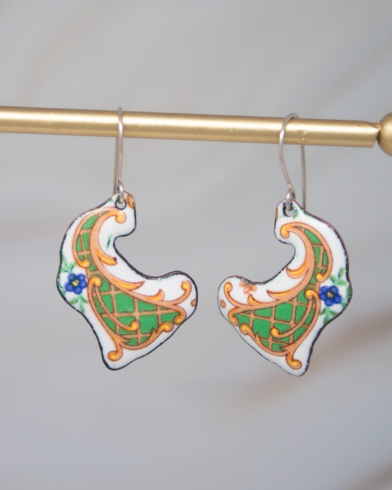 A pair of ornate earrings with intricate designs, hanging from a gold-colored metal hook.