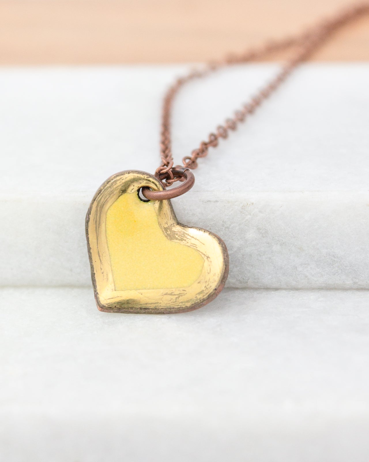 A heart-shaped pendant necklace with a copper-colored metal and a yellowish-brown hue, resting on a white surface.
