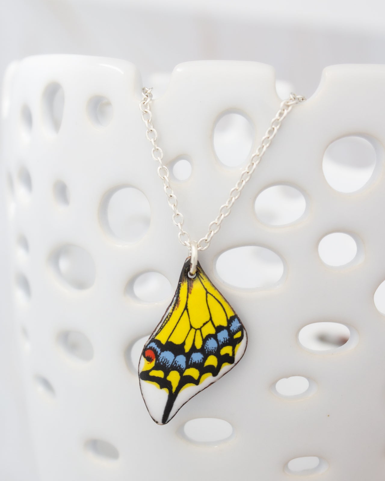 A colorful butterfly wing pendant is hanging from a silver chain against a white background.