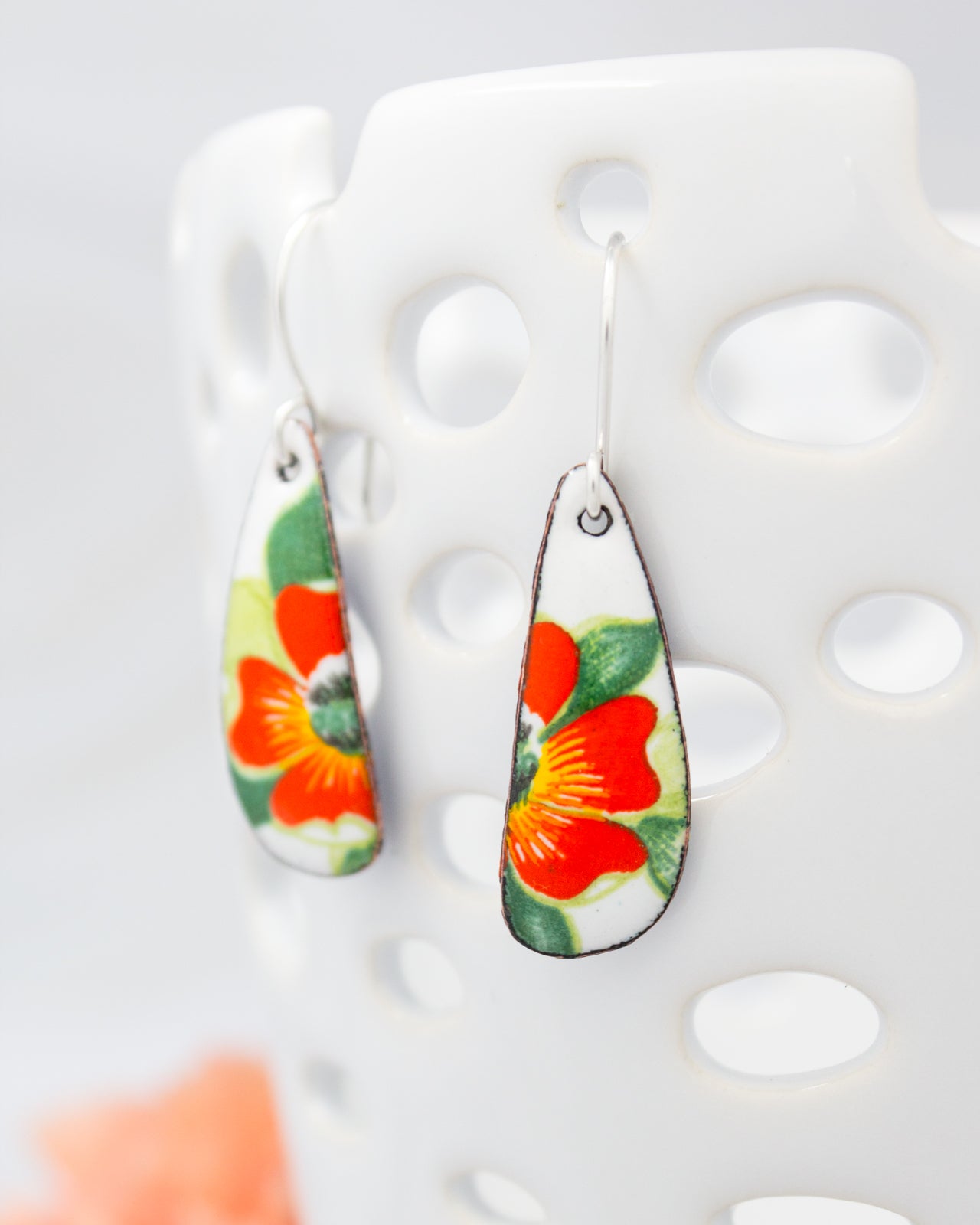 A pair of earrings with a floral design, featuring red and green flowers on a white background.