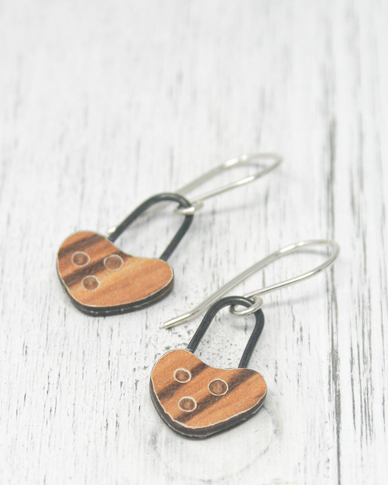 A pair of wooden heart-shaped earrings with black metal hooks, resting on a white wooden surface.