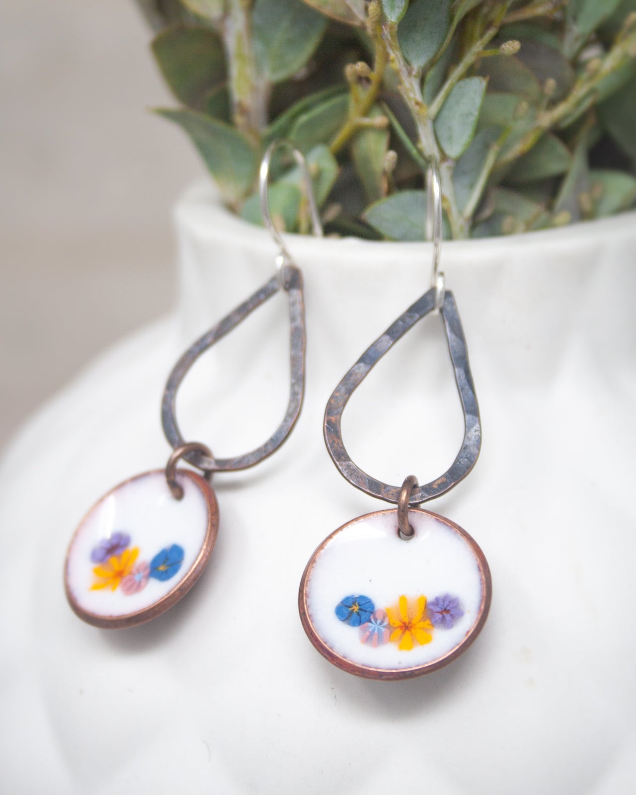 A pair of earrings with a floral design, featuring a white background and colorful flowers.