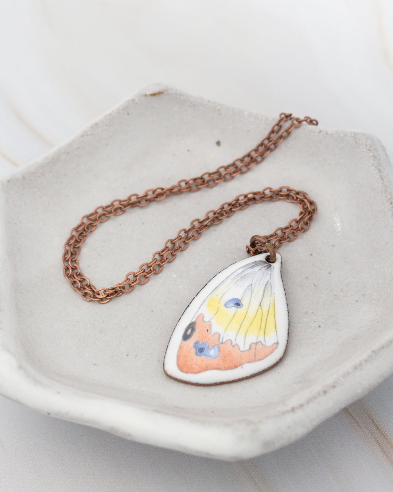 A necklace with a pendant featuring a colorful butterfly design is displayed on a white plate.